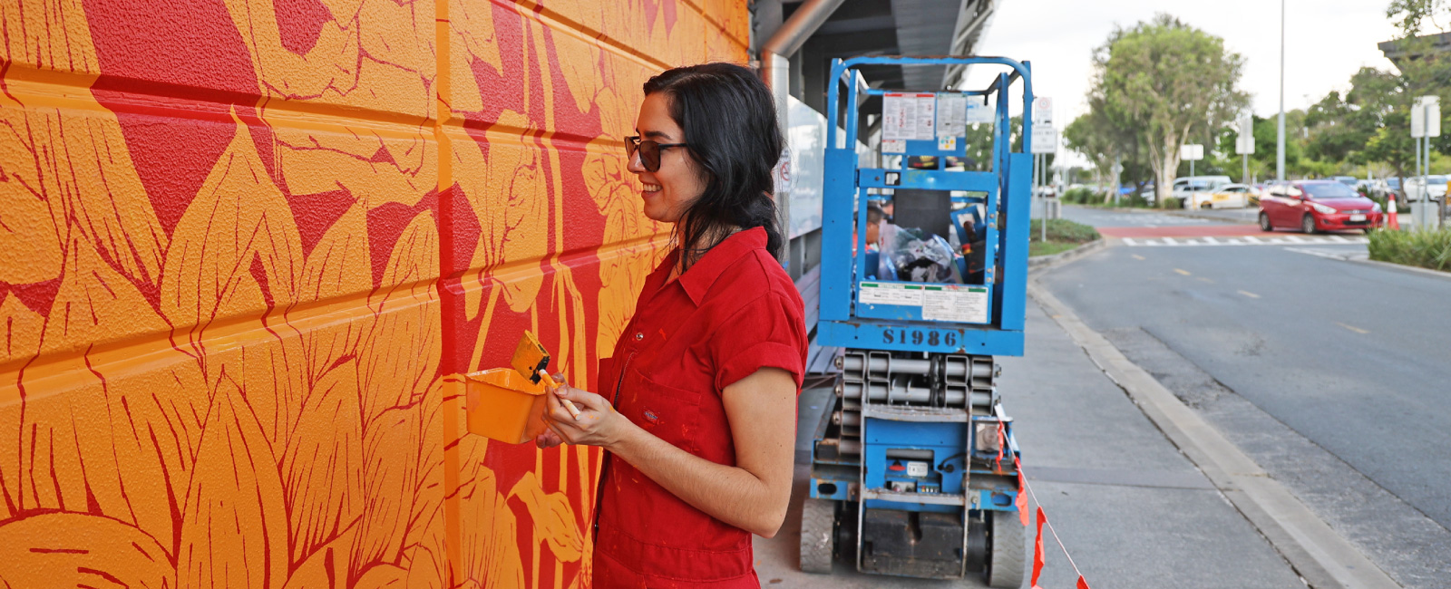 Aurora Campbell painting mural Tangerine Trip, with scissor lift in background