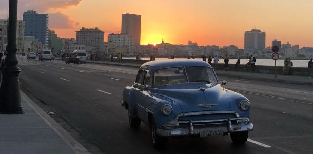 A vintage car on the road with the sun setting behind the city skyline